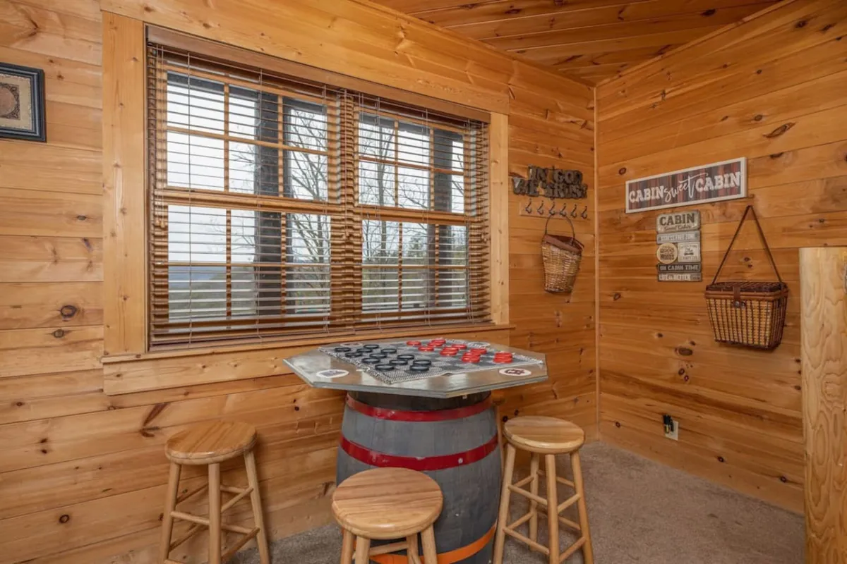 A barrel table set up for a board game, surrounded by wooden walls and a window that lets in natural light. The setting is comfortable and welcoming, ideal for board game battles or quiet moments with family.