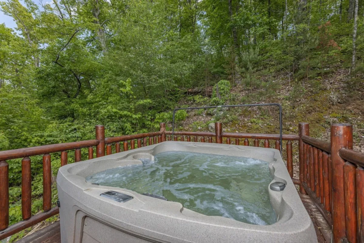 A scenic outdoor hot tub surrounded by greenery and a rustic wooden railing, offering a tranquil spot for relaxation and group conversation amid the natural beauty of the area.