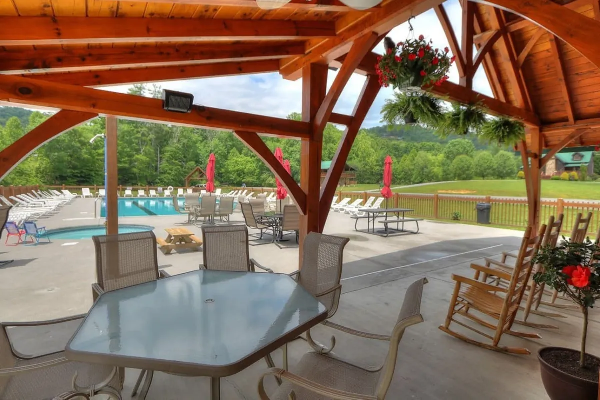 A sparkling swimming pool framed by a covered seating area with rocking chairs, all set before a picturesque mountain landscape. The pool area invites relaxation and social gatherings, with ample space for sunbathing and unwinding after a day of adventure.