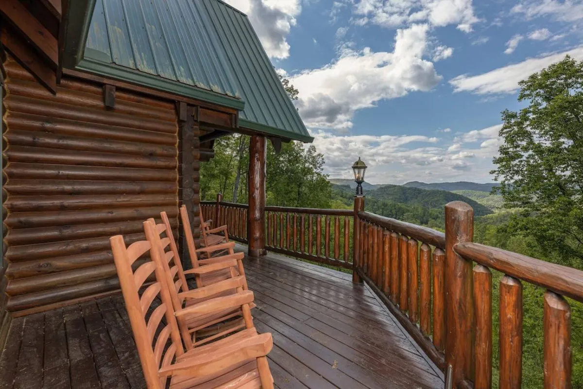 The image showcases the spacious wooden deck of a luxury cabin, with classic rocking chairs lined up along a sturdy railing. The deck overlooks breathtaking, expansive mountain views, creating a serene and inviting atmosphere perfect for relaxation or social gatherings.