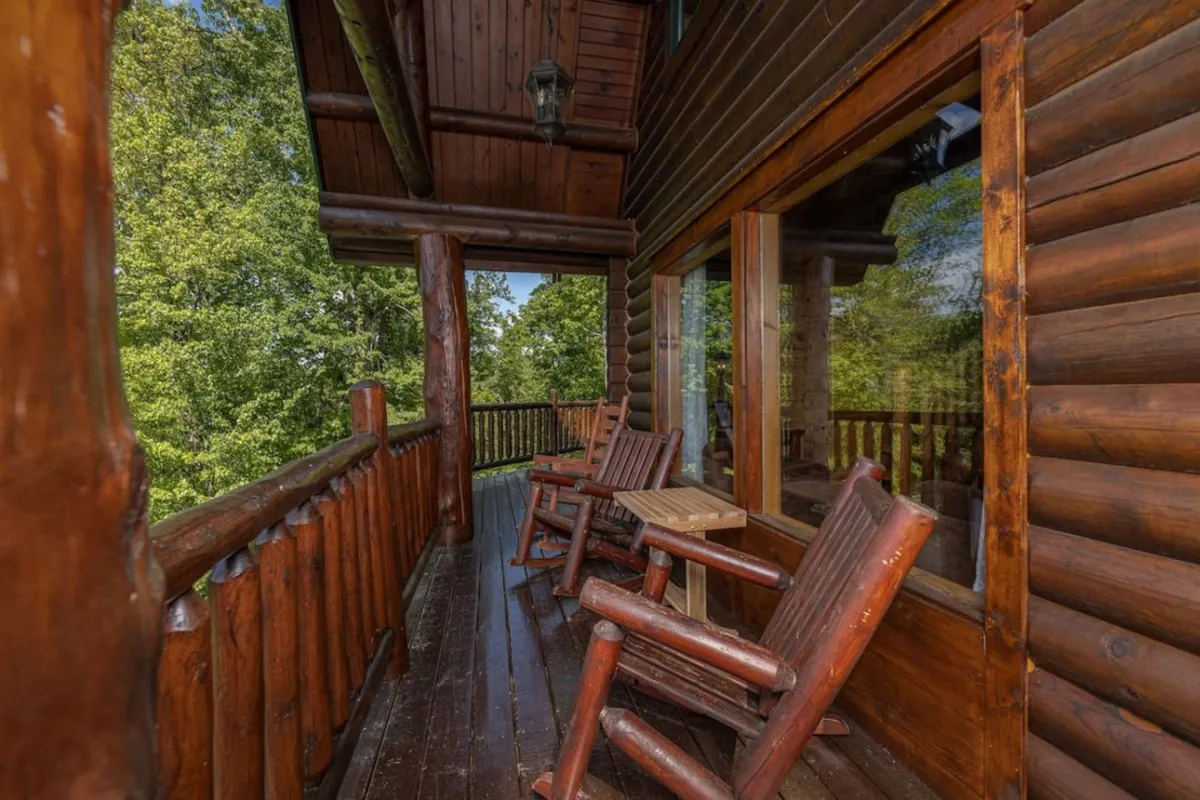 A tranquil porch featuring wooden rocking chairs, a natural wooden railing, and large windows overlooking the forested landscape. The scene is calm and inviting, perfect for coffee at sunrise or relaxing with friends while taking in the view.