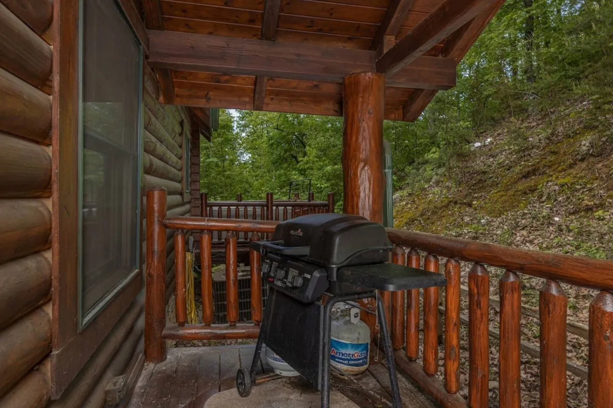 A wooden deck with a grill, sturdy railing, and leafy green surroundings. The setup invites guests to enjoy group barbecues, relaxed outdoor meals, and conversations amidst nature.