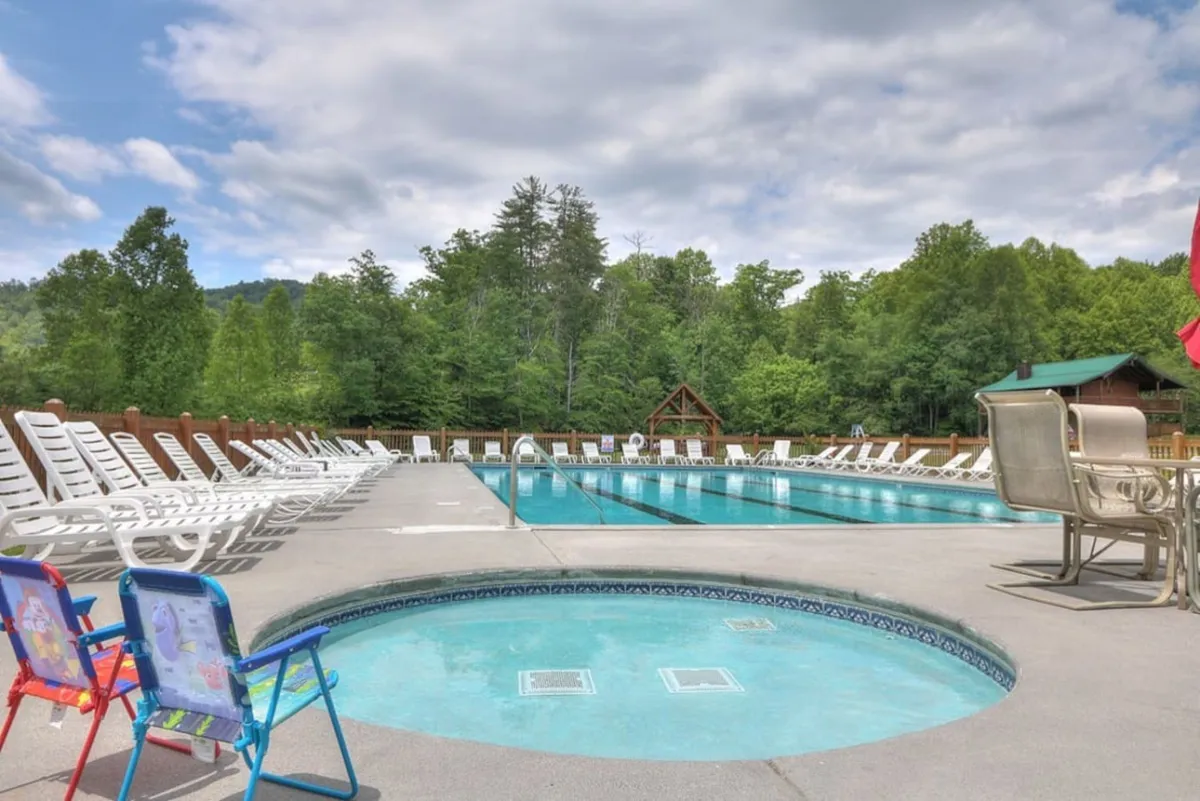 A sparkling swimming pool and hot tub surrounded by lounge chairs and natural greenery. The tranquil setting is ideal for swimming, sunbathing, and family gatherings, with the ambiance promising relaxation and fun during warmer months.